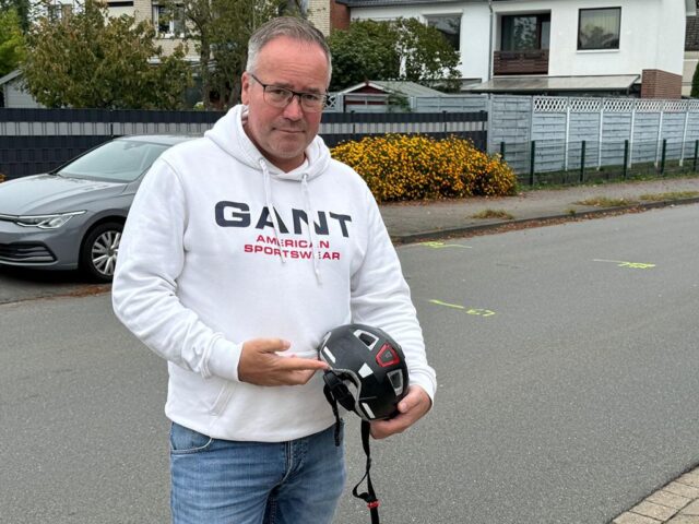 Vater Marco Walczak steht am Unglücksort in der Bürgermeister-Heitmann Straße in Meckelfeld und zeigt auf den Fahrradhelm seines Sohnes. Dieser rettete am Montagnachmittag ein Kinderleben. Foto: Hamann