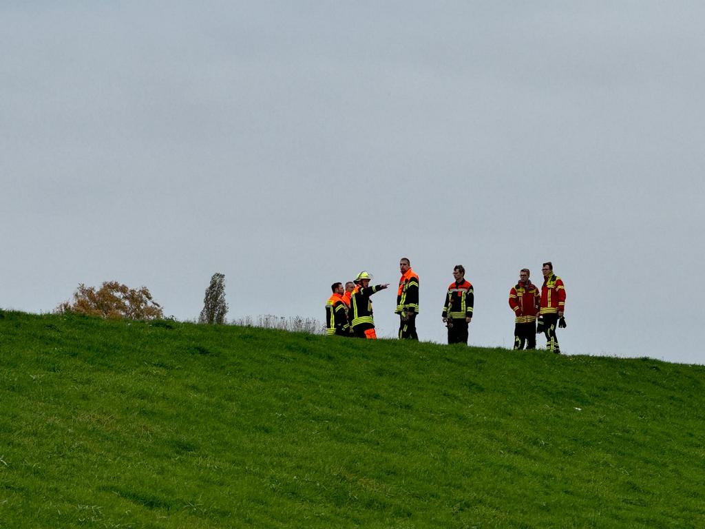 Einsatzkräfte der Feuerwehr besprechen sich auf dem Deich und suchen anschließend das Ufer ab. Foto: Hamann